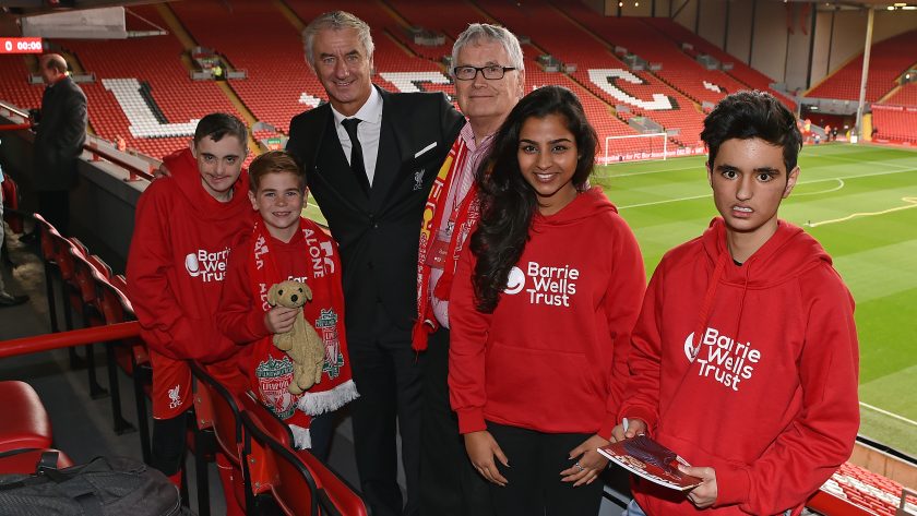 Barrie Wells at a football match, with four children wearing red "Barrie Wells Trust" sweatshirts.