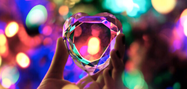 a hand holding a crystal heart with refracted colourful lights